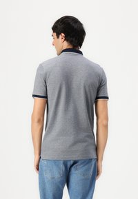 Siva polo majica s tamnoplavim ovratnikom i manžetama, kratkim rukavima i jednostavnim dizajnom. Nosi se uz svijetloplave traperice, prikazano s leđa.