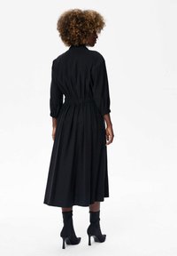 Czarna sukienka z długim rękawem, zebranym w talii, z rozkloszowanym dołem i fakturowanym materiałem. Połączona z czarnymi botkami za kostkę z wydłużonym noskiem.