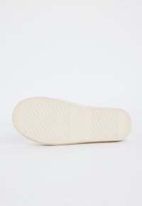 Suela de un zapato beige claro con un patrón de zigzag y un área de agarre texturizada, exhibida sobre un fondo blanco.