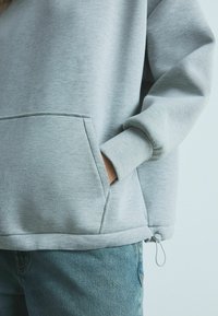Grå sweatshirt med en lomme foran, ribbede manchetter, en snor i kanten og en blød, struktureret overflade, parret med blå jeans.