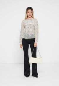 Haut rose clair à manches longues orné de sequins argentés, avec un corsage ajusté et des manches bouffantes, associé à un pantalon noir évasé et un sac à main blanc.