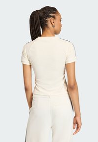 Krémový priliehavý top s krátkym rukávom, ktorý má mäkkú textúru, raglánové rukávy a čierne bočné pruhy. Chrbát je hladký bez ďalších detailov.