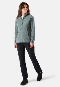 Fleece jacket in muted teal with a full zipper, two side pockets; paired with black cargo pants featuring zippers and pockets, and hiking shoes.