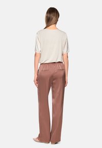 Hellbeiges Kurzarmoberteil mit lockerem Sitz, kombiniert mit weiten, glatten, roséfarbenen Hosen mit elastischem Bund und zwei Gesäßtaschen.