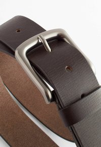 Ceinture en cuir marron avec une surface texturée et plusieurs trous, dotée d'une boucle rectangulaire en métal argenté et d'une face sous-jacente lisse.