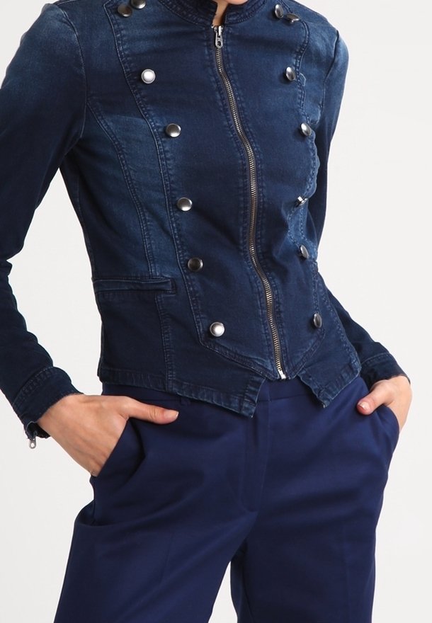 Chaqueta de denim en azul oscuro con un diseño ajustado, cuello alto, botones de presión plateados y cierre con cremallera. Presenta bolsillos laterales y costuras ajustadas.