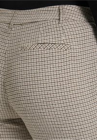 Beige en bruine geruite broek van textuurstof, met een klein achterzakje met een decoratief stikselontwerp.