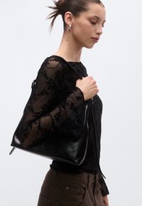 Črna usnjena torbica za ramo z gladkim zaključkom in enojnim trakom za ramo, z zipper zapiranjem in minimalističnim dizajnom.