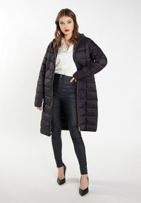 Zwarte pufferjas met capuchon en gouden rits, met een gequilt ontwerp. Gepaarde met zwarte strakke broek en puntige zwarte hakken.