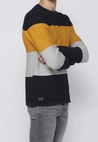 Stickad långärmad tröja med horisontella ränder i marinblått, senapsgult, grått och vitt. Har en ribbad textur och en liten logotyp patch.