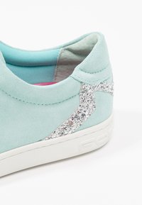 Sneaker in suede azzurro chiaro con un accento di glitter argento testurizzato, suola in gomma bianca e foderatura rosa visibile all'interno della scarpa.
