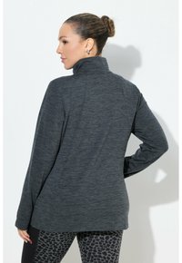 Giacca sportiva grigio scuro con colletto alto, maniche lunghe e tessuto texture. Abbinata a leggings neri con stampa leopardata.