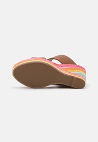 Sandalia de cuña con una tira de cuero marrón, parte superior tejida multicolor y suela de goma texturizada. La base presenta franjas vibrantes en rosa, amarillo y azul.