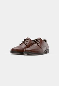 Chaussures en cuir marron à lacets avec une finition lisse, des orteils arrondis et un petit talon empilé. Détails de couture discrets sur le dessus.