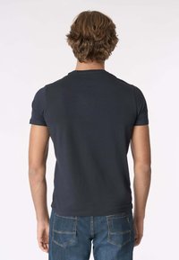 T-shirt nera a maniche corte con scollo rotondo, tessuto liscio e design aderente. Indossata con jeans di denim blu, vista da dietro.