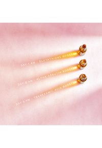 Drei Glasfläschchen mit Tropfern in bernsteinfarbener Farbe, auf einem sanften rosa Hintergrund platziert. Textetiketten zeigen die Booster-Typen für verschiedene Tage an.