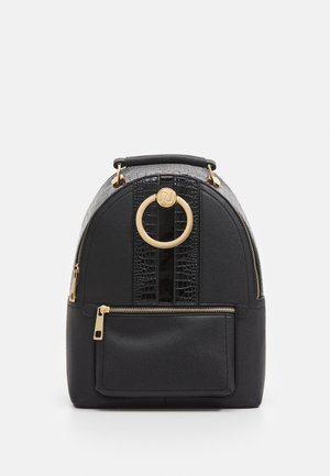 Sac à dos noir texturé avec une poche avant zippée, des détails de fermeture éclair dorée, une poignée supérieure et une décoration en anneau circulaire doré sur le devant.