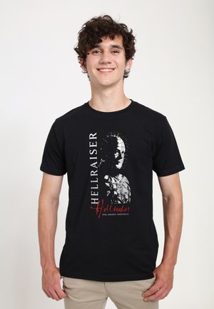 Sort bomulds t-shirt med et grafisk print af en karakters ansigt med spidse detaljer. Teksten inkluderer "Hellraiser" og "Hellseeker."