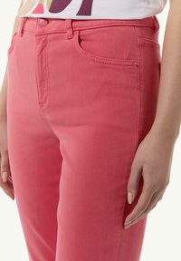 Jasnoróżowe dżinsy o gładkiej fakturze, z zapięciem na guzik, przednimi kieszeniami oraz detalami szwów wzdłuż krawędzi.