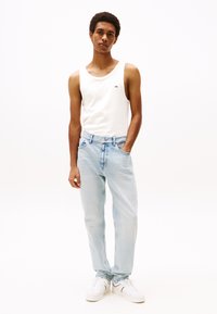 Lyseblå denimjeans med avslappet passform, kombinert med en hvit ermeløs tanktopp. Hvite sneakers fullfører antrekket.