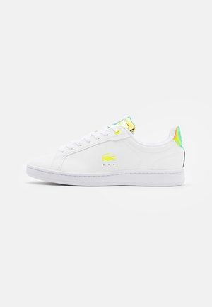 Baskets basses blanches avec logo crocodile jaune, languette et languette de talon iridescents, et semelle blanche sur fond blanc.