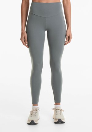 Leggings atletice de culoare gri deschis cu talie înaltă, realizate dintr-un material elastic. Acestea au o textura netedă și un design ajustat. Sunt purtate cu adidași ușori.