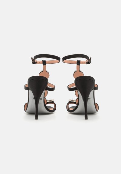 Melnas papēžu sandales ar elegantu dizainu, kurām ir šauri siksniņas, potītes sprādzes un stiletto papēdis. Gluda āda un metāliski akcenti.