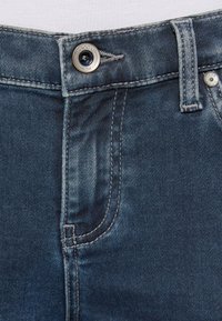 Dark blue denim jeans featuring contrast stitching, a silver button closure, and a subtle worn texture near the zipper area.