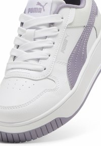 Sapatilhas brancas de couro com detalhes em roxo claro, apresentando um design texturizado, bico redondo e solado de borracha com padrões de aderência.