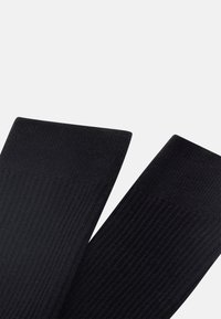 Juodos raižytos kojinės, pasižyminčios lygiu paviršiumi ir vienodu dizainu, su šiek tiek sustiprinta viršutine kraštine papildomam patvarumui.