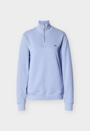 Lichtblauwe sweater met ritssluiting, geribbelde structuur en een hoge hals. Heeft een klein geborduurd logo op de borst. Zachte stof.