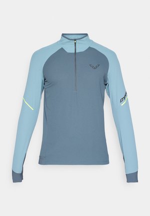 Pull-over zippé à manches longues en deux tons de bleu, avec un col haut, un tissu texturé et des accents réfléchissants sur les manches.
