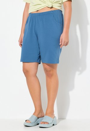 Blaue, knielange Shorts aus weichem Stoff mit einem elastischen Bund und Seitentaschen, kombiniert mit hellblauen, offenen Plattform-Slides.