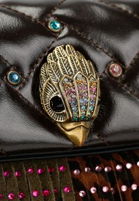 Clutch in pelle marrone con motivo trapuntato, dotata di un fermaglio a forma di uccello in tonalità dorata decorato con pietre preziose colorate e arricchito con borchie rosa e blu.