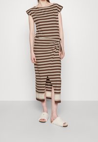 Brązowa i kremowa w paski bawełniana sukienka, długości do kolan, z bocznym węzłem i rozcięciem. Nosić z białymi, puszystymi klapkami.