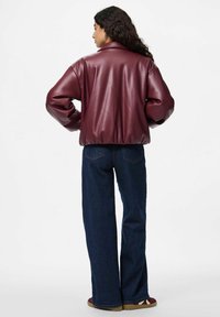 Burgunderfärgad faux läderjacka med rund hals, oversized passform och ribbat midjeband, i kombination med mörkblå vida jeans och avslappnade skor.