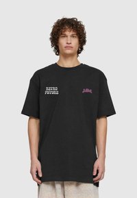 Melna kokvilnas T-kreklu ar uzrakstu "RETRO FUTURE" baltā krāsā un rozā grafiku labajā pusē. Brīvs piegriezums un īsas piedurknes.