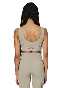 Beżowy stanik sportowy z dekoltem w serek, z logo "ATW" na dole. Gładki, elastyczny materiał, uzupełniony pasującymi legginsami z wysokim stanem.