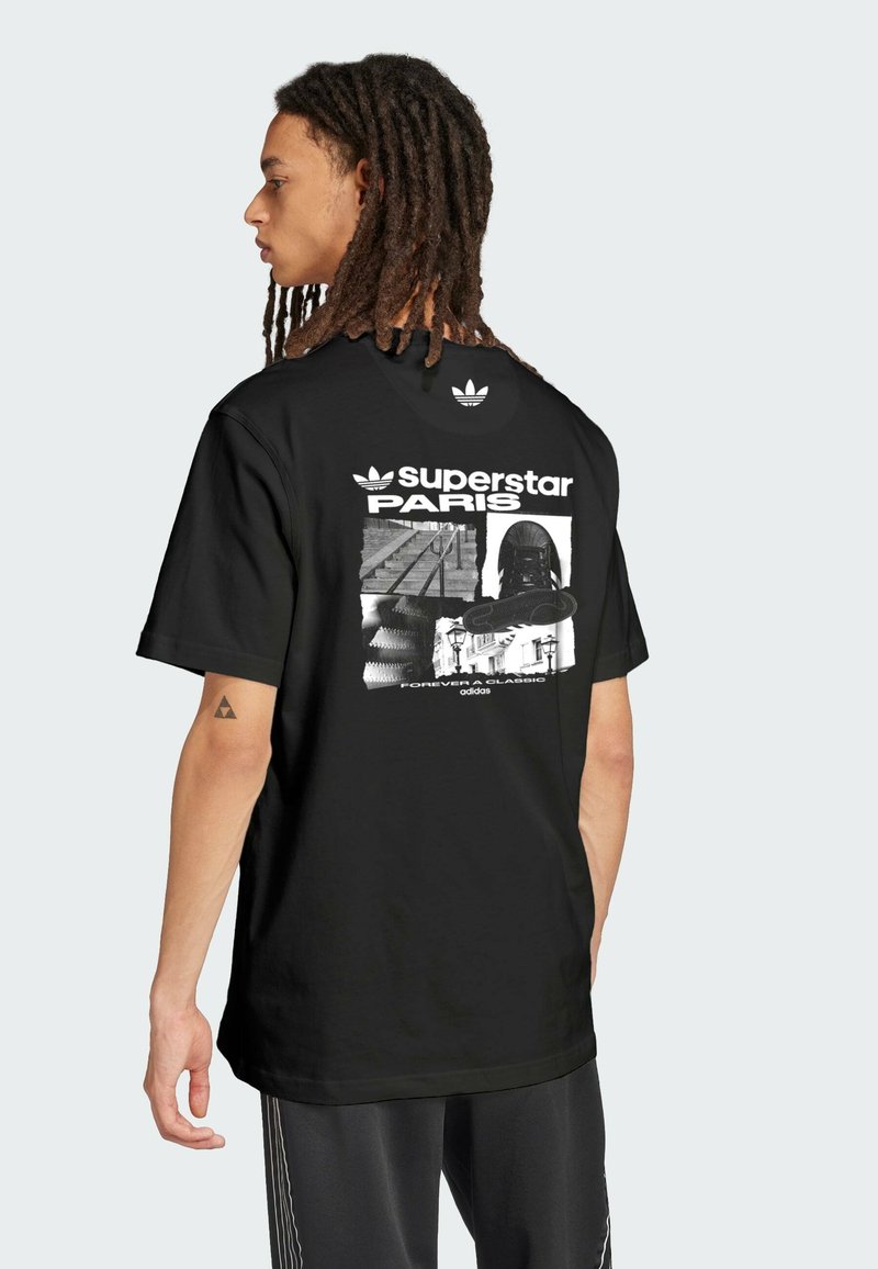 Black cotton t-shirt featuring a graphic print on the back with “superstar PARIS” text, and Adidas logo. Short sleeves, crew neck design.