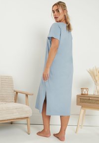 Vaaleansininen, polvipituinen mekko, jossa on lyhyet hihat, sivureikä ja pehmeä kangas, jota henkilö käyttää paljain jaloin.