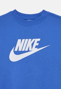 Modrá bavlnená tričko s výrazným bielym logom Nike a dizajnom swoosh. Hladký a jemný povrch, rebrovaný golier.