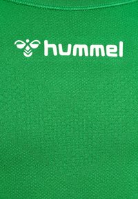 Grön sporttröja gjord av texturerad tyg, med en vit logotyp "hummel" och en emblem ovanför texten. Rund halsringning.