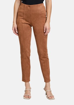 Rostfarbene Wildlederhosen mit hohem Bund, taillierter Passform und vertikalen Nähten. Kombiniert mit minimalen beigen Sandalen.