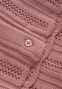 Rosa stickad tyg med texturerade mönster och en glänsande rund knapp med fyra hål, som visar en mjuk och detaljerad design.