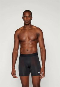 Férfi fekete sportnadrág légáteresztő anyagból, testhezálló szabással, rugalmas derékpánttal és fehér Nike logóval.