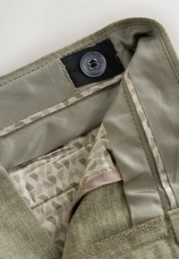 Close-up of garment waistband showing a button on an adjustable black elastic band and patterned beige fabric lining.