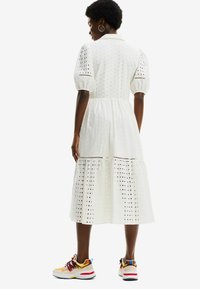 Abito bianco in cotone con design ad occhiello ricamato, maniche a sbuffo corte e gonna a strati. Abbinate a sneakers atletiche colorate.