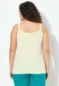 Top giallo chiaro senza maniche con spalline sottili e scollatura arrotondata, realizzato in un tessuto morbido, abbinato a pantaloni blu-verdi.