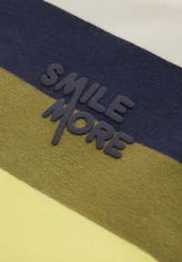 T-tröja i bomull med horisontella ränder i marinblått, olivgrönt och gult. Har upphöjd text "SMILE MORE" i mörkblått.