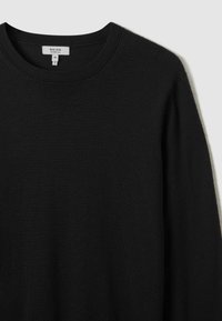 Pull noir à manches longues avec un décolleté rond, fabriqué à partir d'un tissu doux. Présente une étiquette avec le nom de la marque et la taille, design minimaliste.